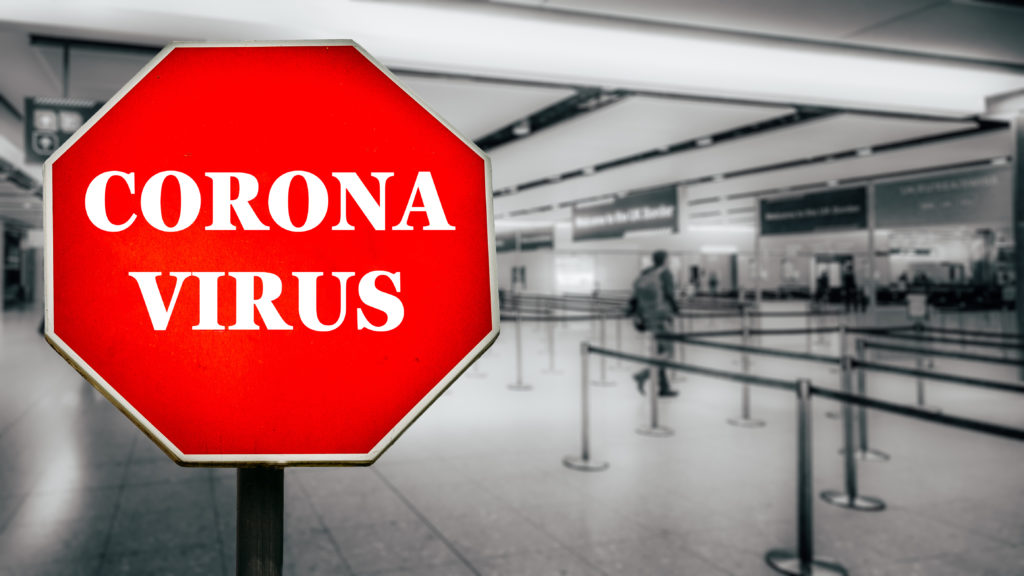 Coronovirus written on stop sign with passengers arriving at passport control within generic airport. The virus, which originated in China is quickly spreading around the world in early 2020